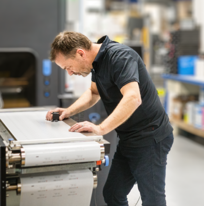 Hombre operando una máquina de impresión de etiquetas en un entorno de producción.